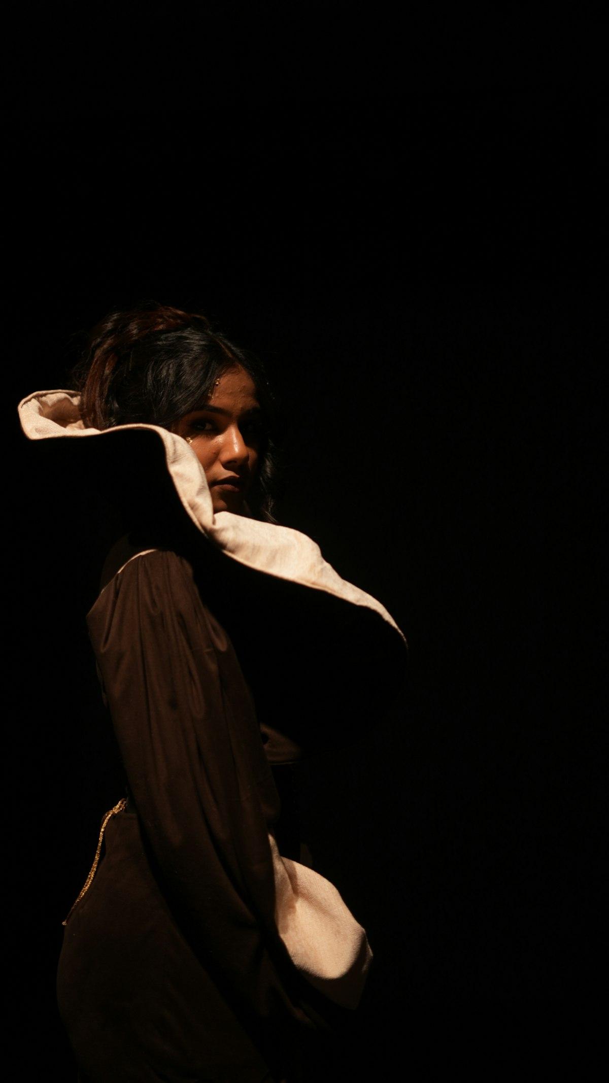 A model turning into a warm spotlight against a near-black backdrop.